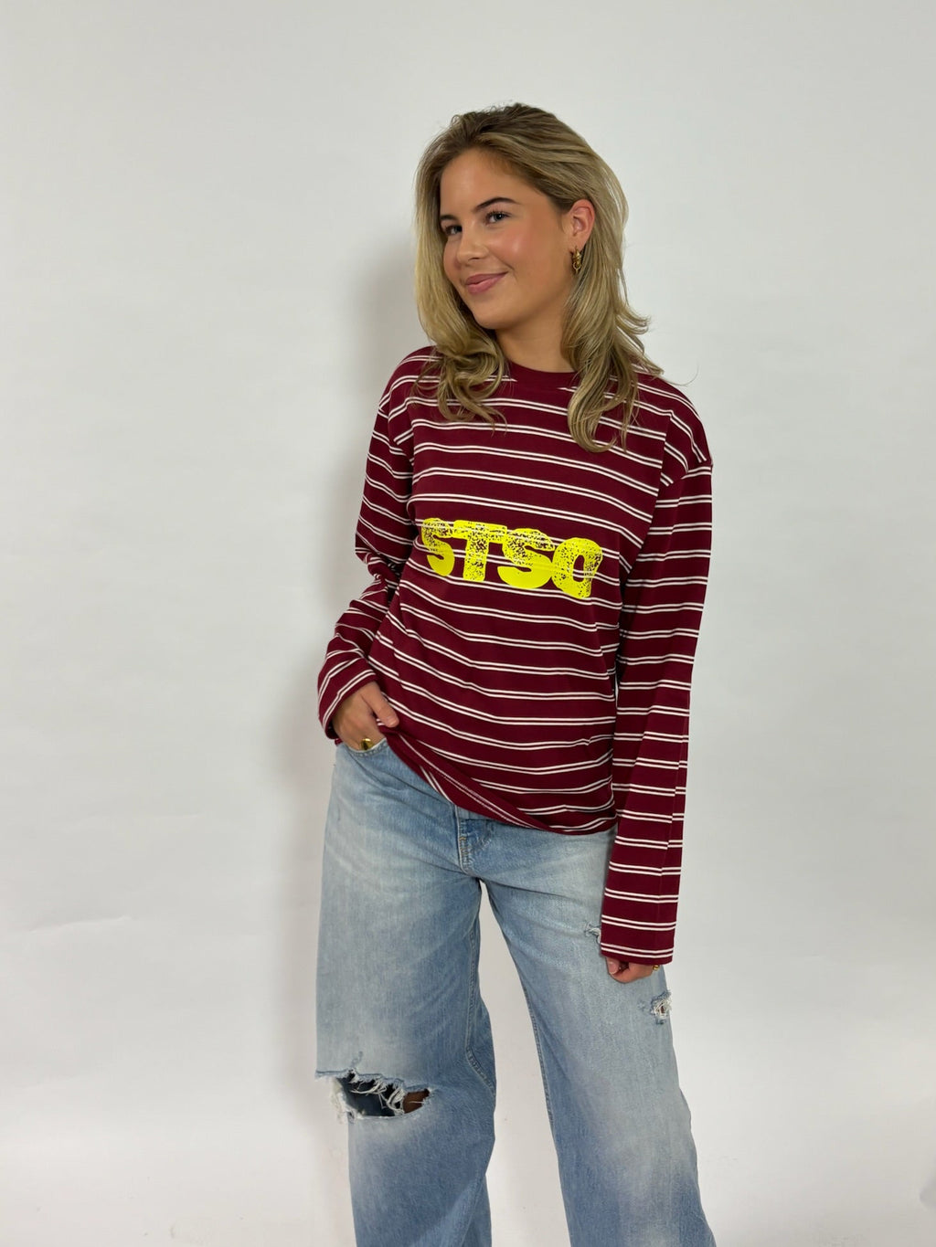 Gestreepte longsleeve bordeaux met gele STSO van 72.71 Clothing – voorkant, gedragen door een vrouwelijk model met een lichte jeans