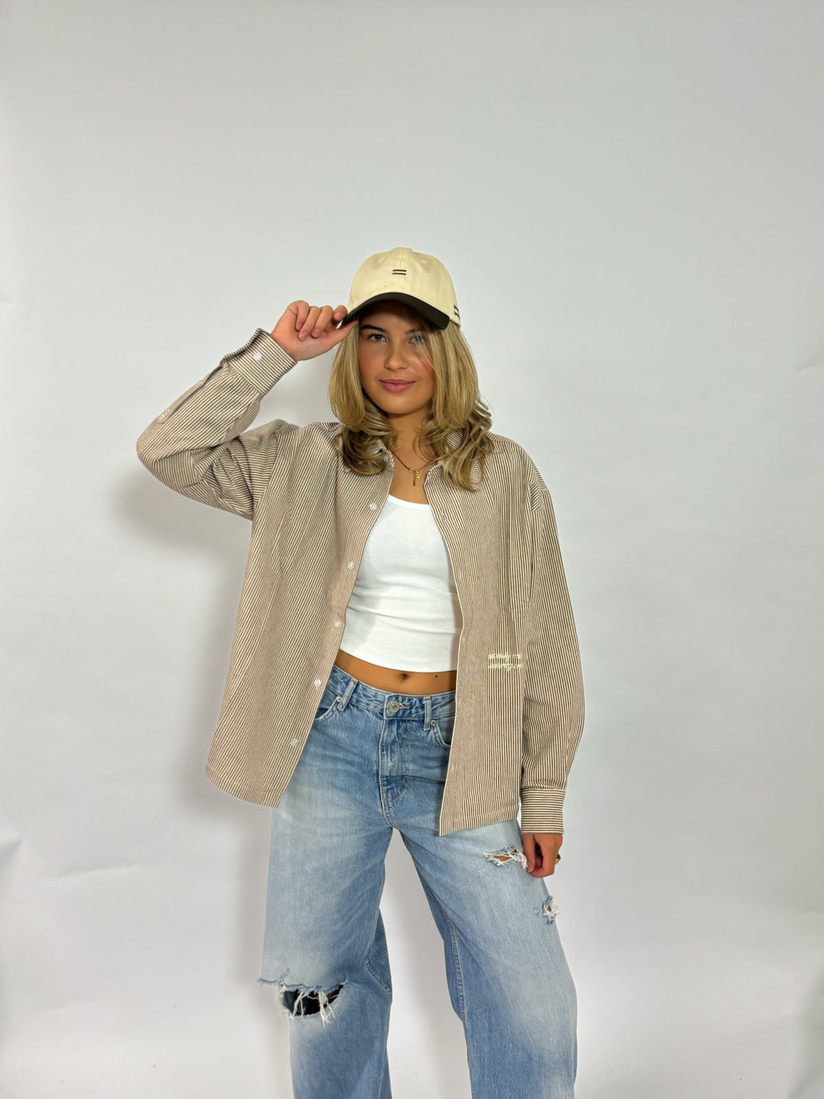 Cap crème met donkerbruine klep van 72.71 Clothing – gedragen door een vrouwelijk model met een overshirt en jeans