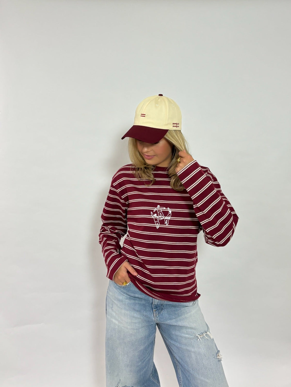 Cap crème met bordeaux klep van 72.71 Clothing – gedragen door een vrouwelijk model met een gestreepte longsleeve