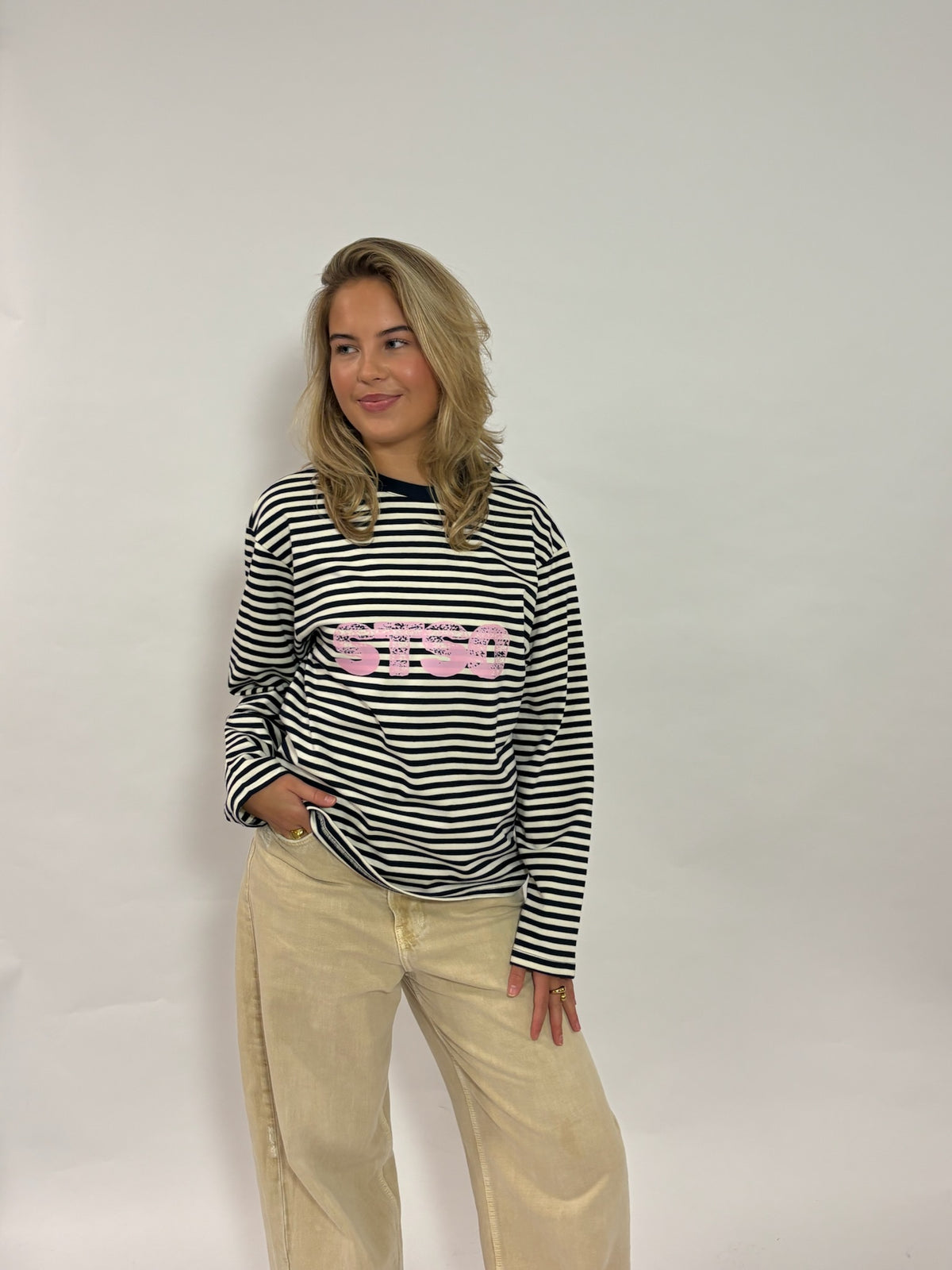 Gestreepte longsleeve navy met roze STSO van 72.71 Clothing – voorkant, gedragen door een vrouwelijk model met een beige broek
